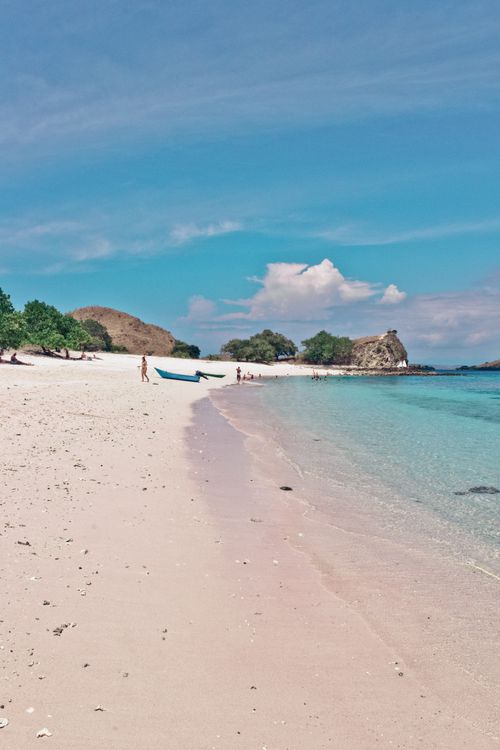 Free A serene tropical beach with clear water, blue skies, and lush greenery. Stock Photo