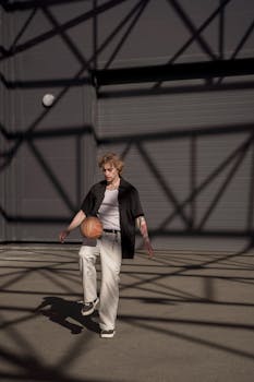 Young man playing basketball outdoors, casting a dynamic shadow on urban concrete.