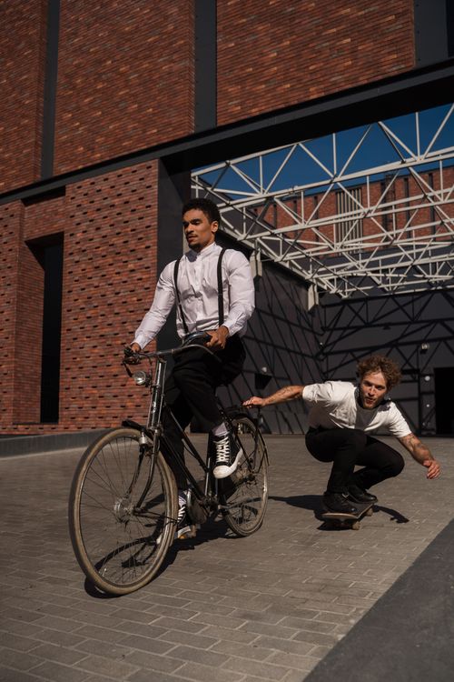 Free Two adults in action, a cyclist on vintage bike and a skateboarder, in an industrial urban setting. Stock Photo