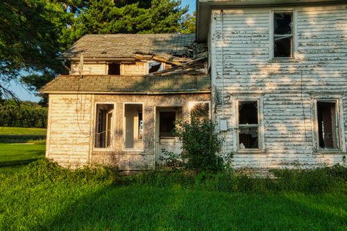 Free Old, decaying wooden house set in a lush green field, captured at sunset. Stock Photo