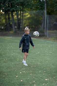 A young boy is focused on playing soccer on a green field, wearing a black jacket and white socks.