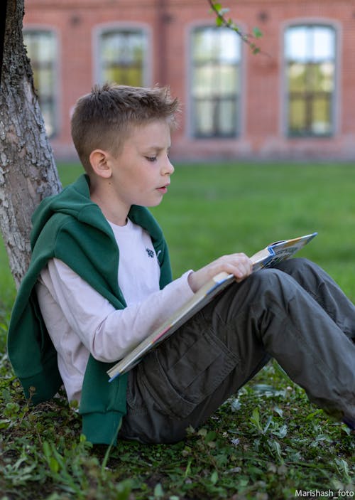 Free Boy Sitting on the Ground While Reading a Book Stock Photo