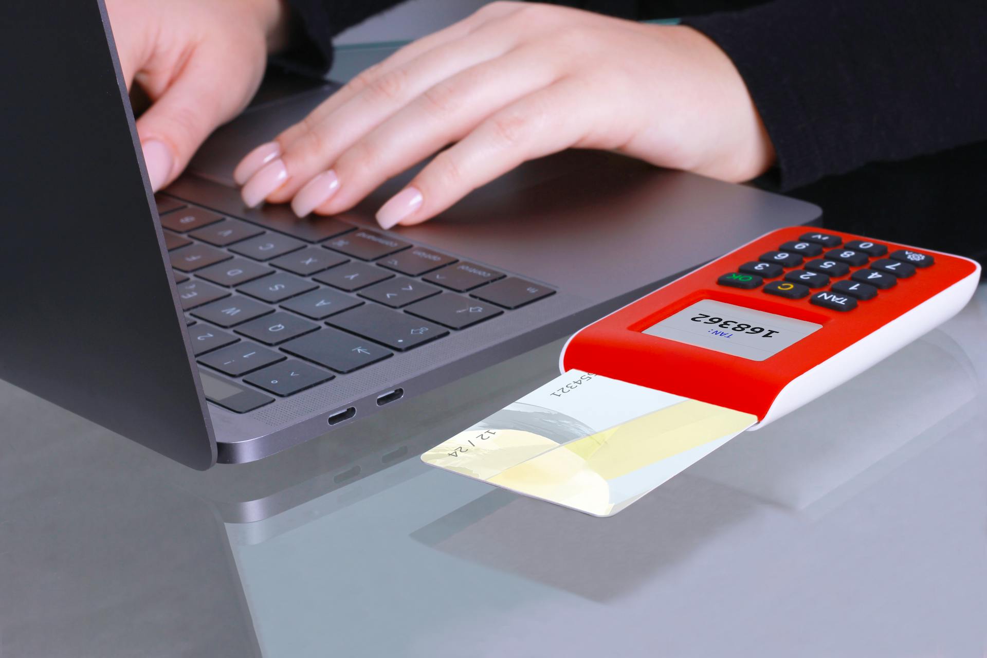 Close-up of hands using laptop and card reader for online payment.