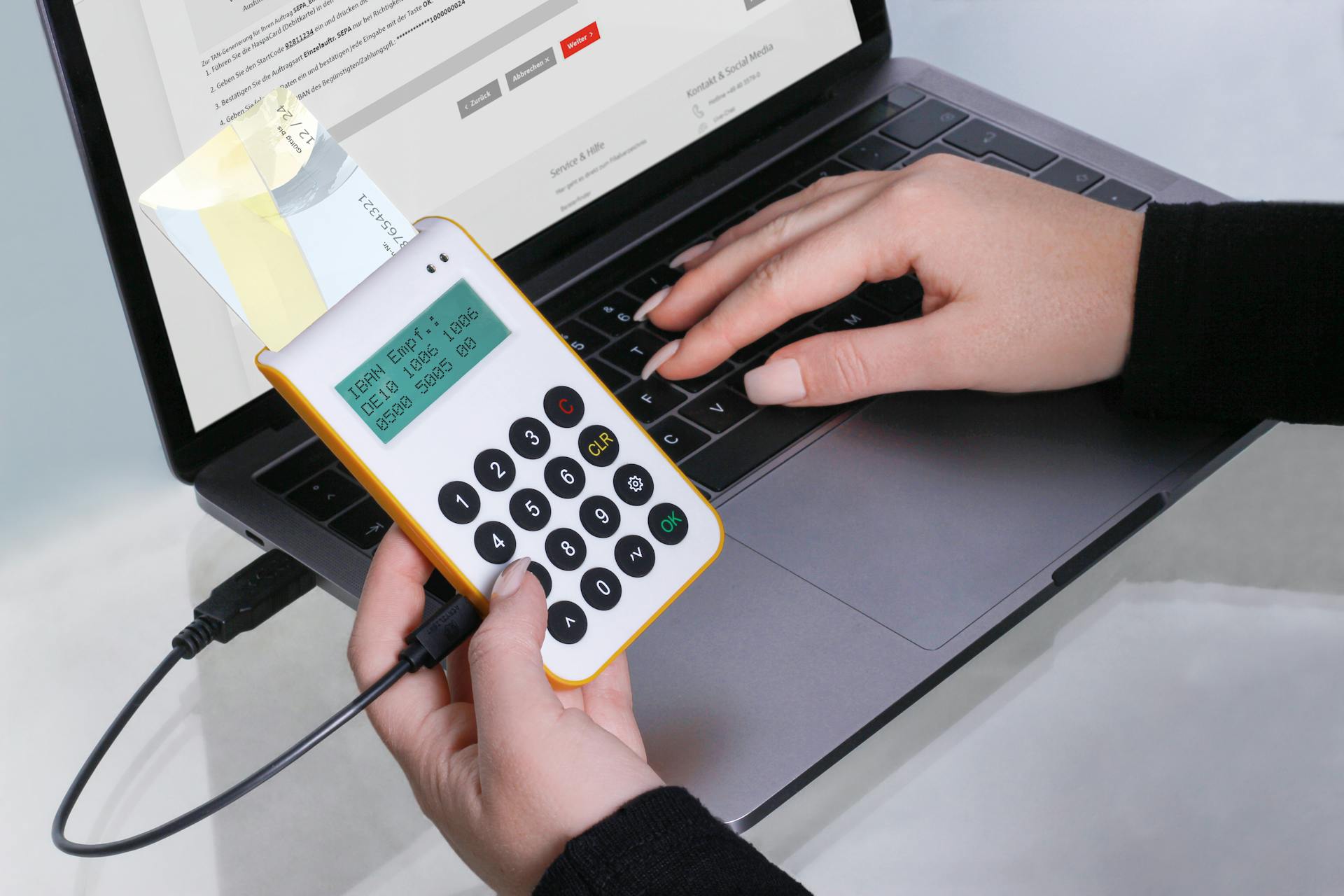 Close-up of hands using a card reader for online transactions via laptop, showcasing cashless payment technology.