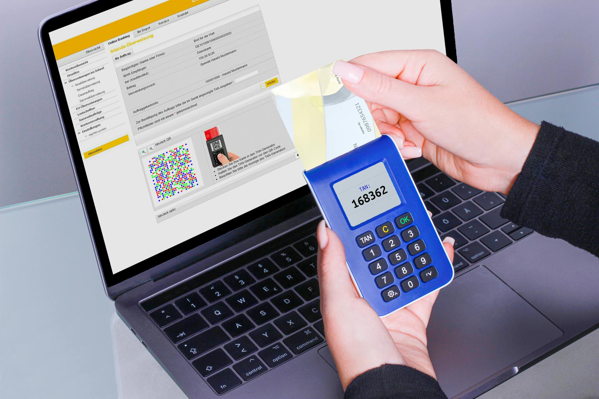 Hands using a TAN generator next to a laptop for secure online banking transactions.