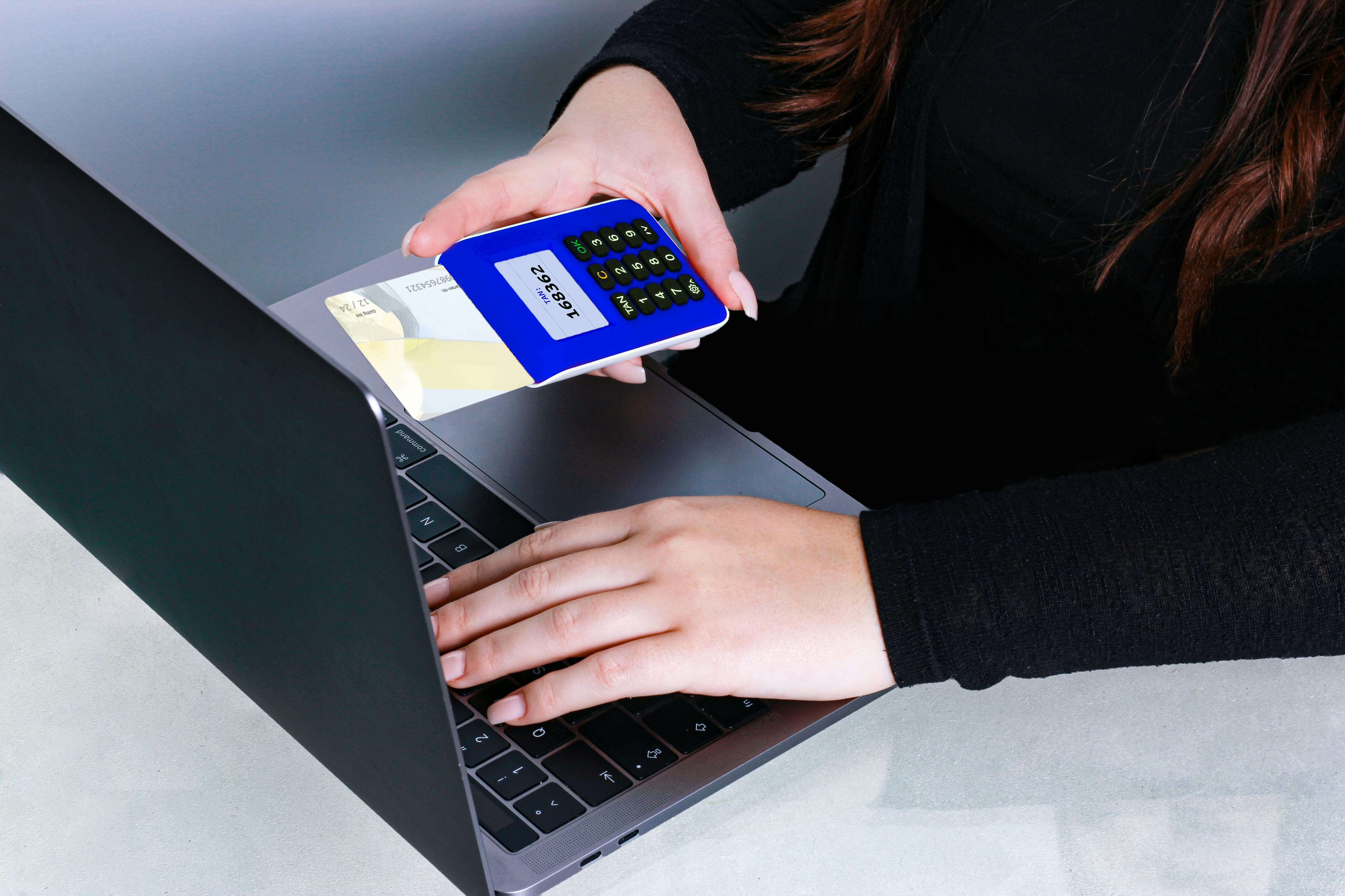 a person in black long sleeves holding a pos device with card while typing on a laptop