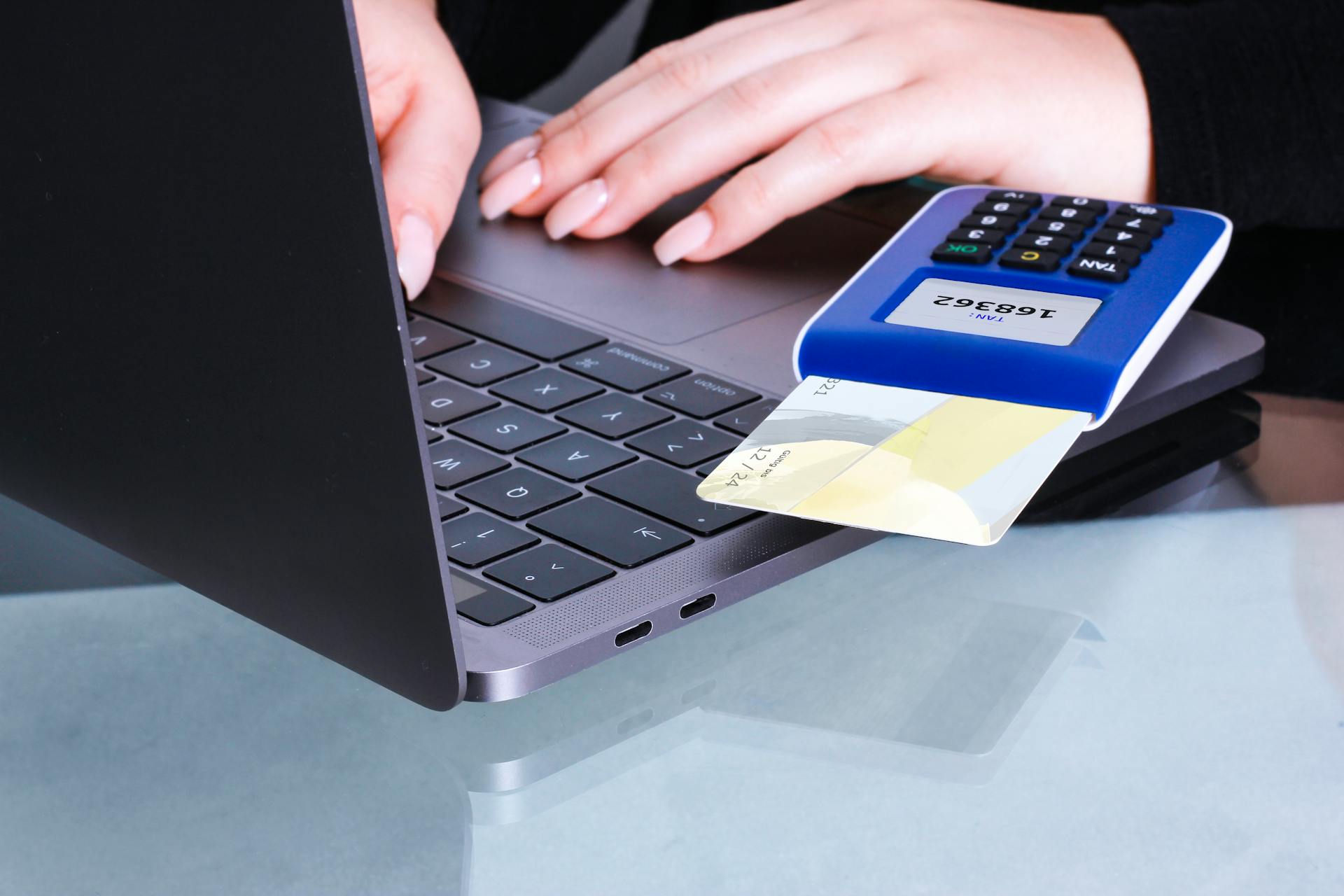 Hands performing a contactless payment using a laptop and card reader for online transaction.