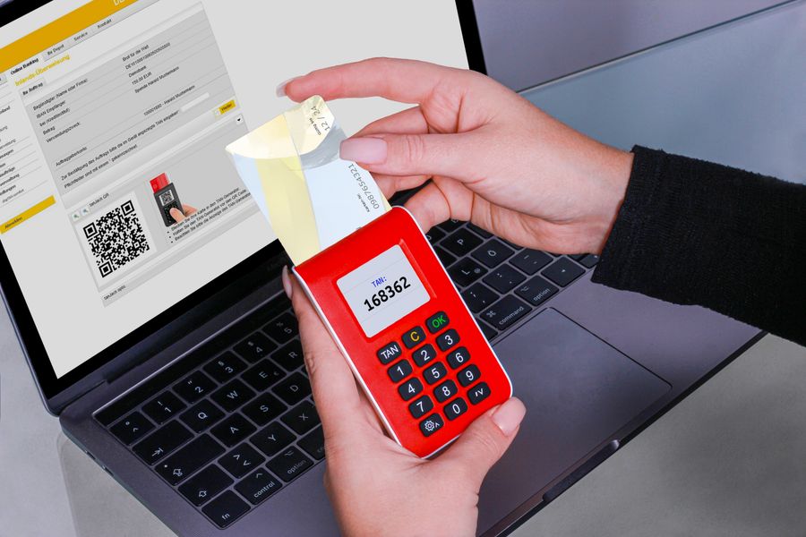 A hand holding a one-time-code generator displaying a code in front of a laptop login screen