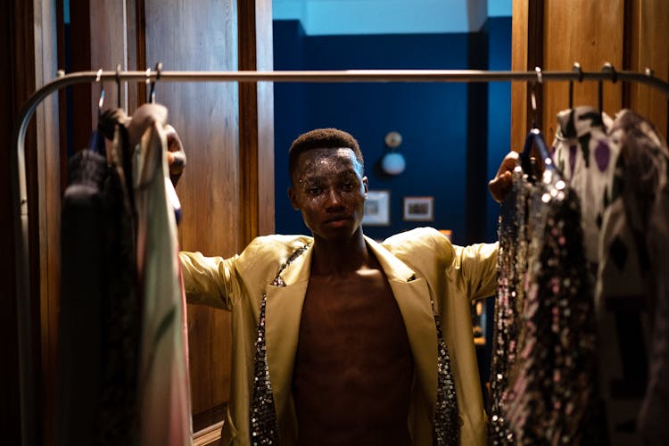 Man In Satin Yellow Jacket Standing Between Clothes In Stylist Wardrobe