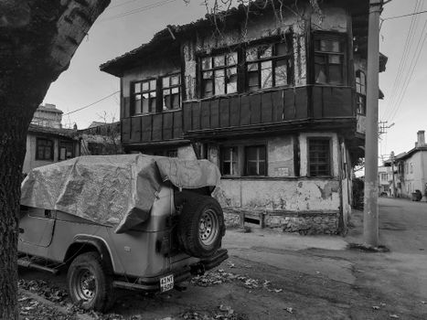 Black and white photo of a rustic street with an old vehicle and historic house.