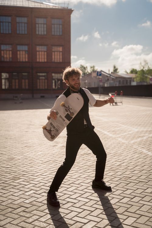 Free A bearded man joyfully holding a skateboard outside a building on a sunny day. Stock Photo