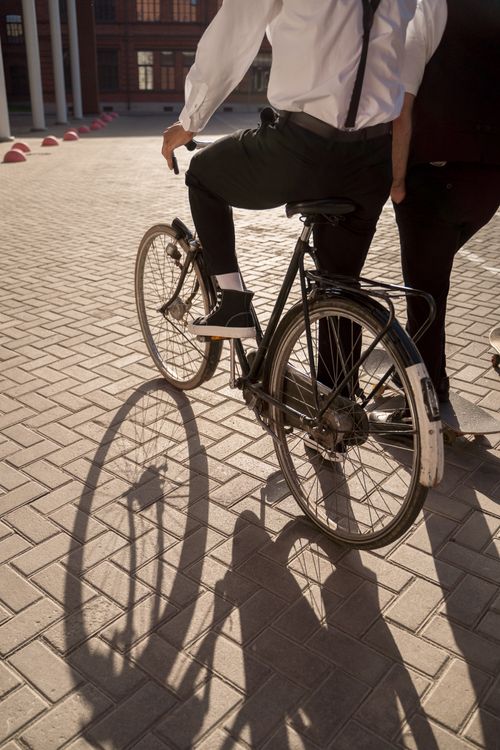 Free Elegant cyclist wearing stylish attire riding a bicycle on a street with shadows cast. Stock Photo