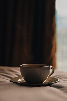 A steaming cup of coffee on a saucer, set against a warm, cozy background.