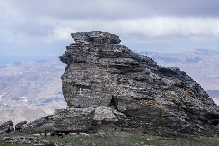 Flock Of Sheep Walking Under Large Rock Formation In Mountains