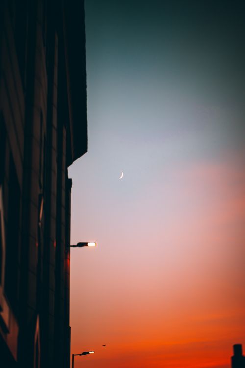 Free A crescent moon shines in a colorful twilight sky above an urban cityscape silhouette. Stock Photo