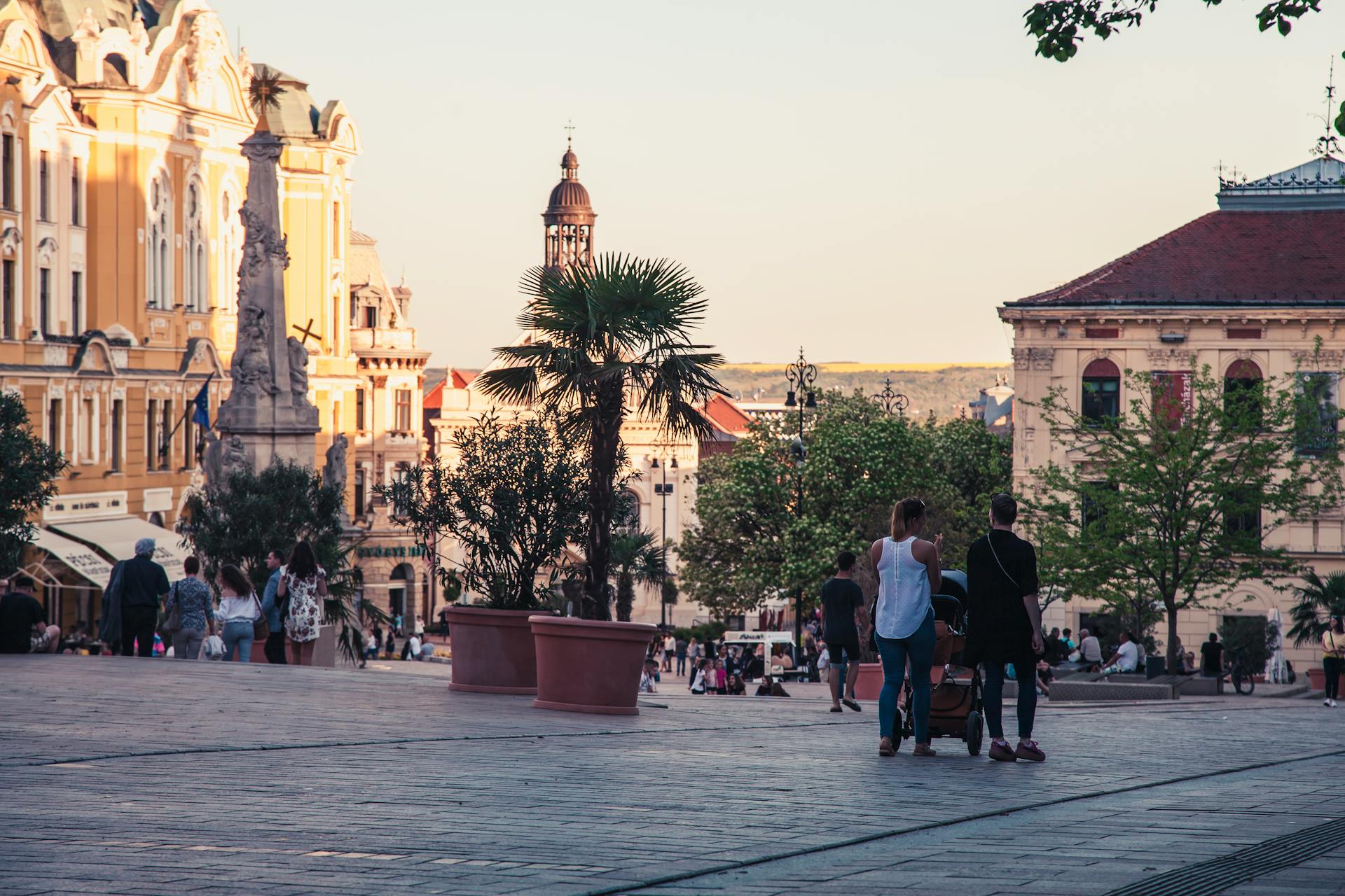 People enjoy a beautiful city square surrounded by historic architecture at sunset.