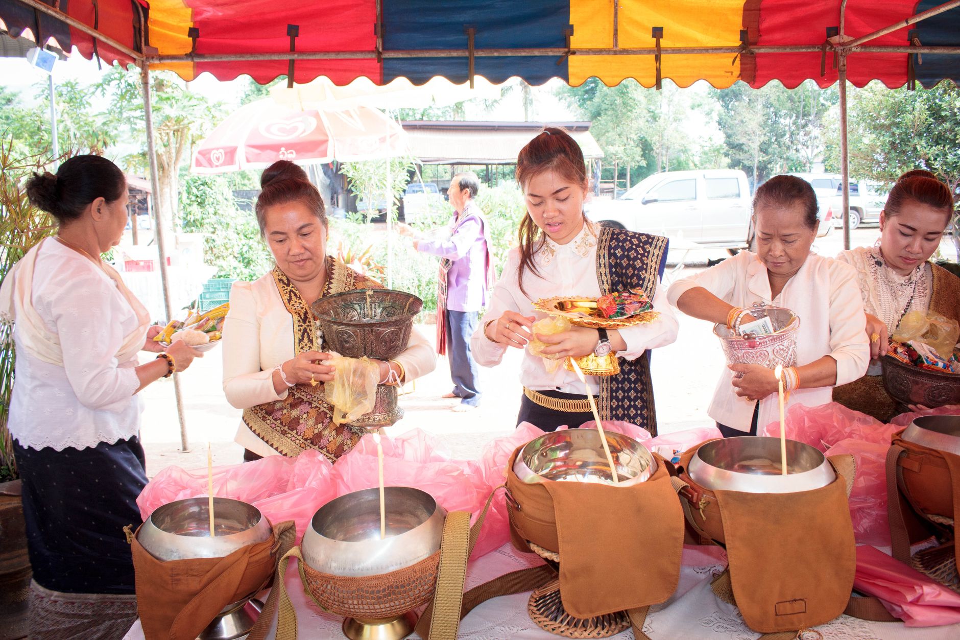 Women in traditional Lao attire participate in an outdoor offering ceremony, showcasing cultural heritage.