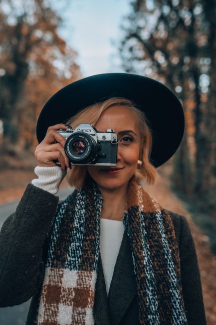 Stylish woman holding a vintage camera outdoors in an autumn scene, showcasing a warm and artistic mood.