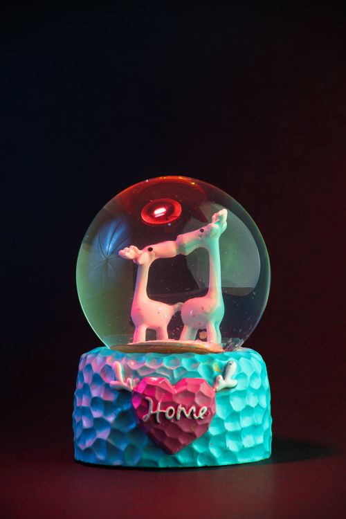 Free Vibrant snow globe featuring kissing giraffes, illuminated against a black background. Stock Photo