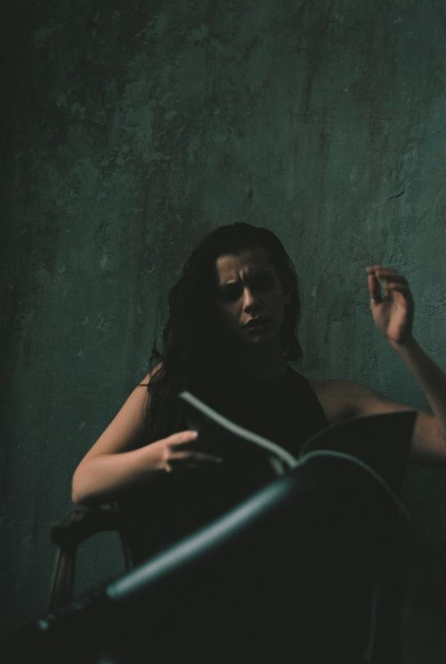 Free A woman in a black top reads in a dramatic, dark ambiance, conveying introspection and mystery. Stock Photo