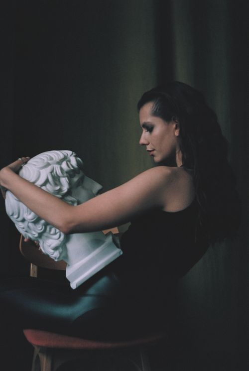 Free A woman in a dark setting holding a classical sculpture head, side view. Stock Photo
