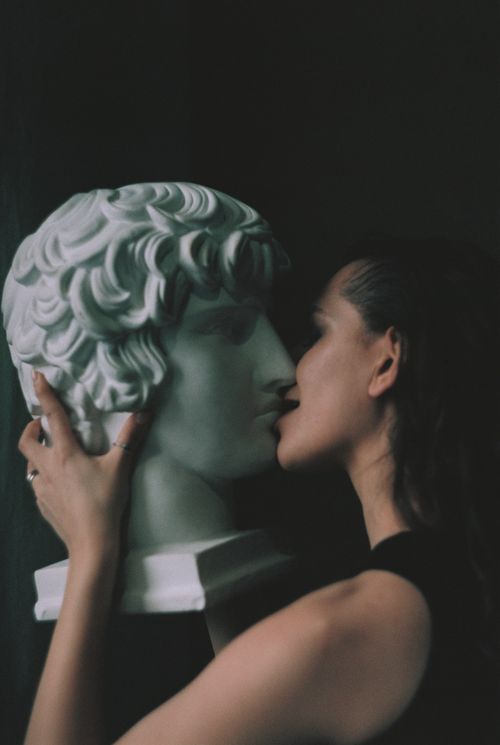 Free A woman elegantly kisses a marble sculpture against a dark backdrop, blending art and emotion. Stock Photo