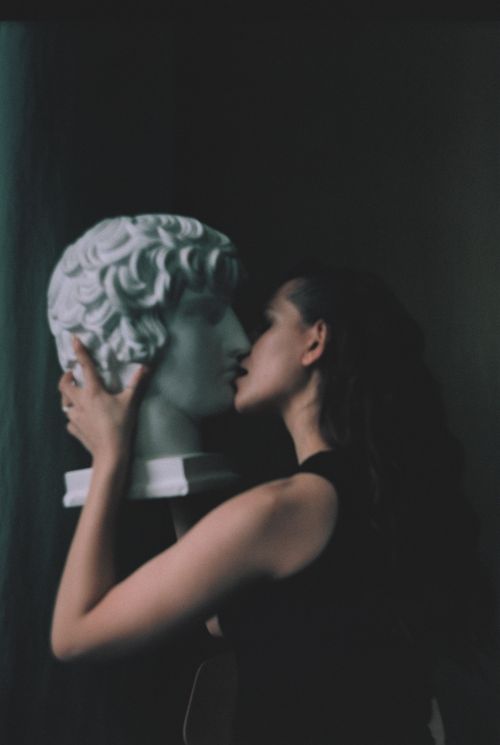 Free A creative and moody portrait of a woman embracing and kissing a classical bust sculpture. Stock Photo
