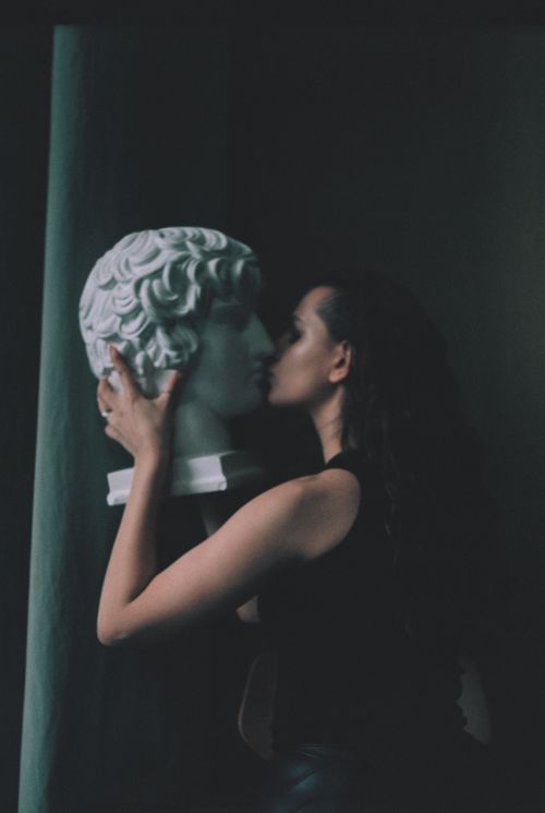 Free A woman passionately kisses a classical sculpture in a dimly lit indoor setting. Stock Photo