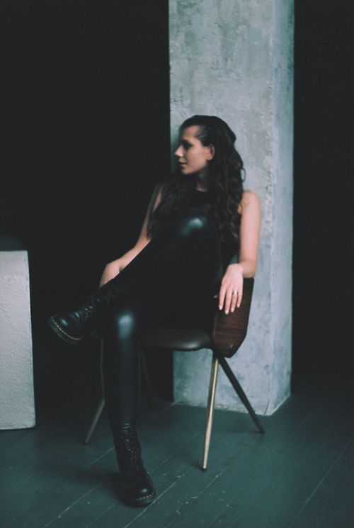 Free Stylish portrait of a woman in black leather attire sitting on a chair in a dark, minimalist setting. Stock Photo