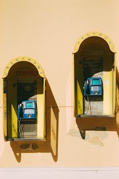 Two vintage public telephones on a sunny yellow wall in Zakynthos, Greece.