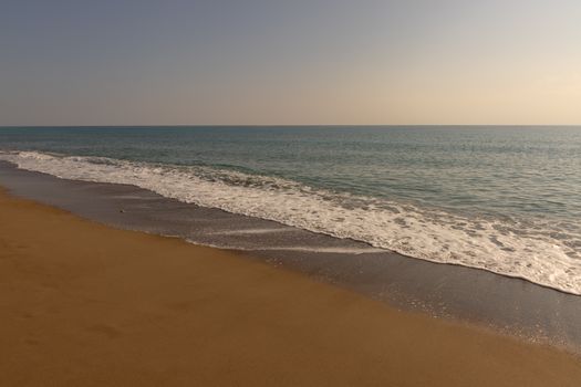 A peaceful beach scene with gentle waves lapping against a sandy shore under a clear sky.