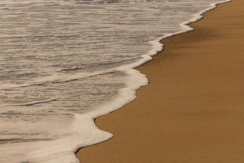 Free Peaceful coastal scene of waves gently washing over a golden sandy beach. Stock Photo