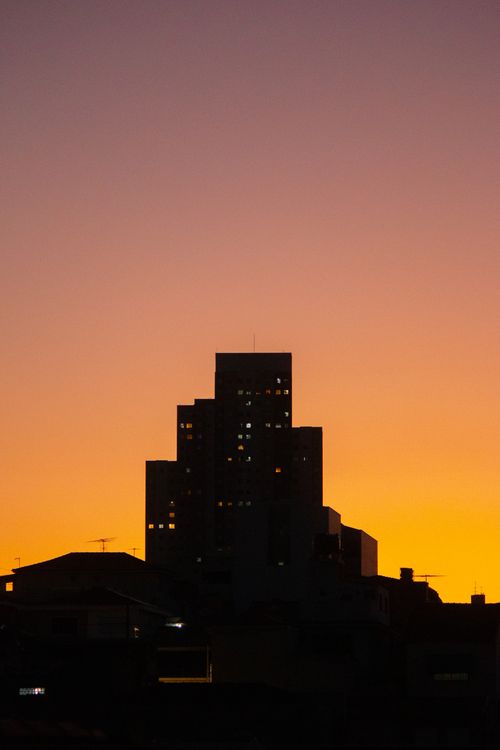 Free Silhouette of a city skyline against a vibrant orange sunset sky, featuring a prominent building tower. Stock Photo
