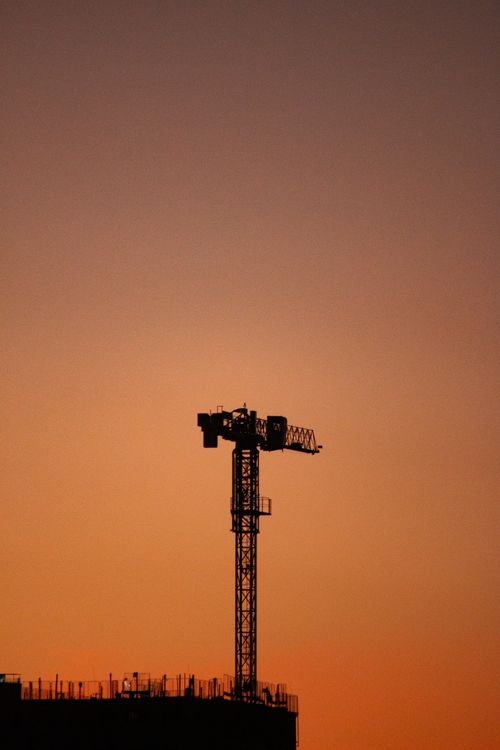 Free A tower crane silhouetted against a colorful sunset sky at a construction site. Stock Photo