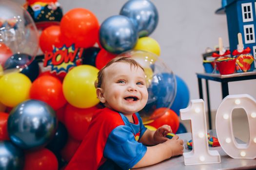 A smiling child at a colorful superhero themed birthday celebration with balloons and decorations.