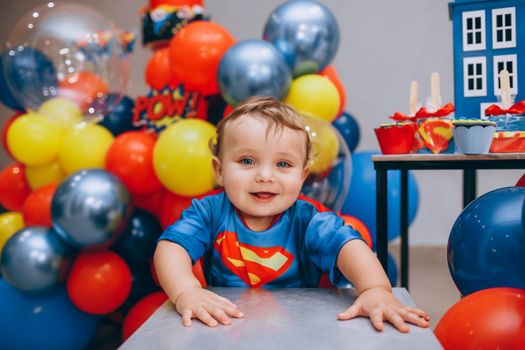 Adorable toddler enjoying a colorful superhero-themed birthday party with balloons and decorations.