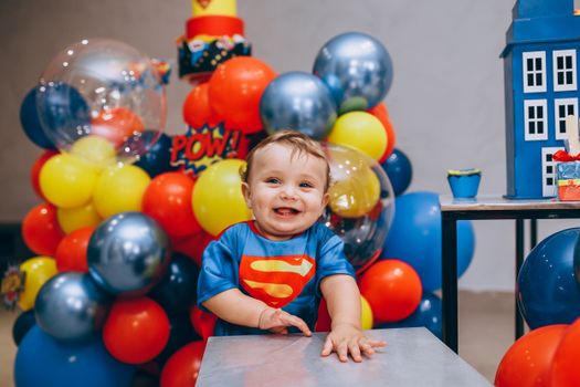 Delighted baby enjoying a colorful superhero-themed birthday party with balloons and decorations.