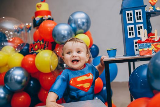 A cheerful toddler in a superhero costume enjoying a vibrant birthday party with colorful balloons and decorations.