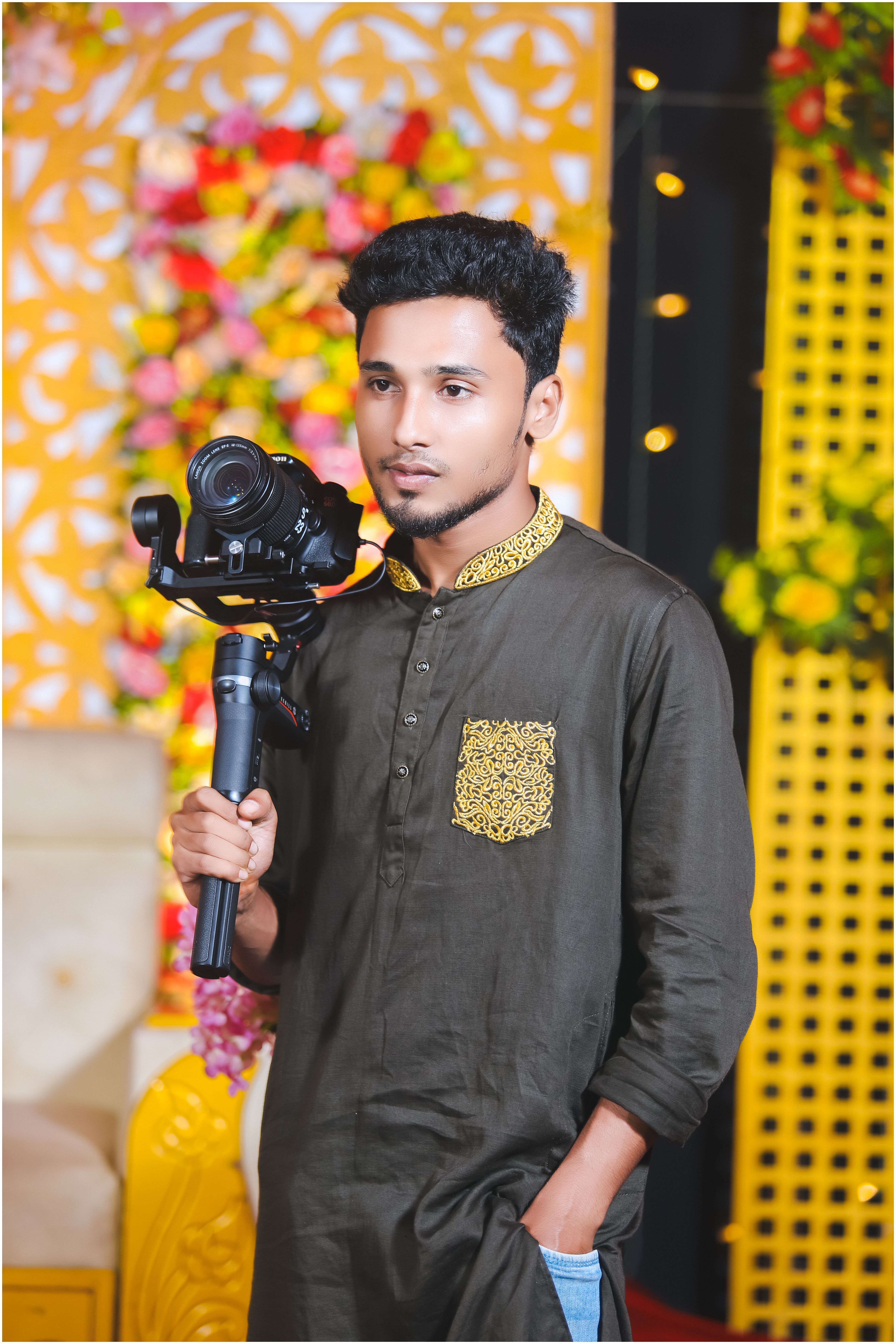 Young Bangladeshi photographer using a gimbal indoors with floral backdrop.