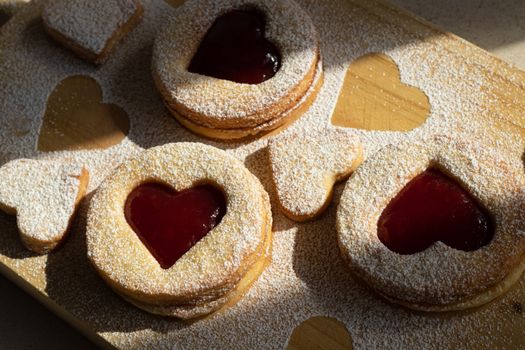 Delicious heart-shaped jam cookies with powdered sugar on a wooden board, perfect for special occasions.