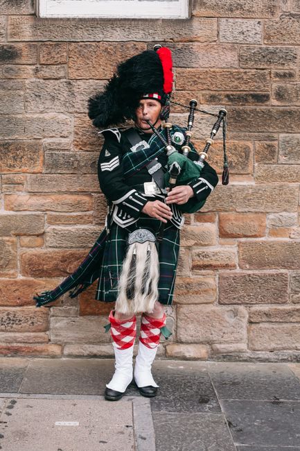 Scottish bagpiper playing music on the streets of Edinburgh, wearing classic attire and kilt.