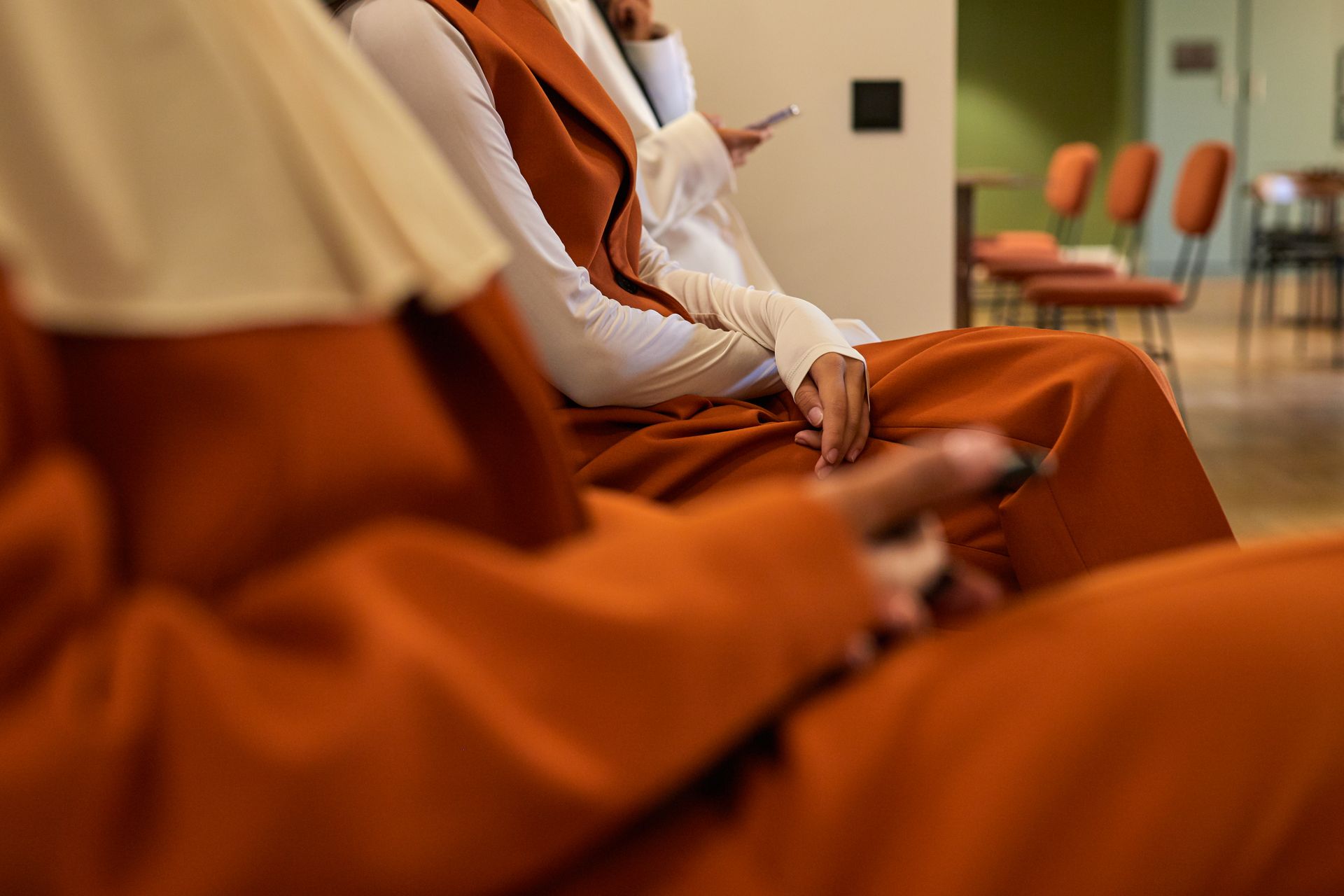 Three women in hijabs using smartphones in a modern office setting.