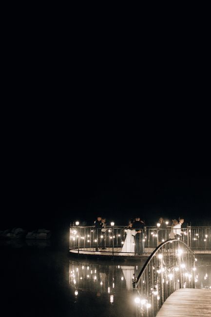 A romantic nighttime wedding with couples on a beautifully illuminated bridge reflecting in water.