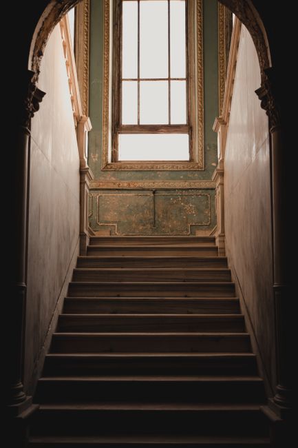 A beautifully aged staircase leading to a majestic window, showcasing classic architecture.