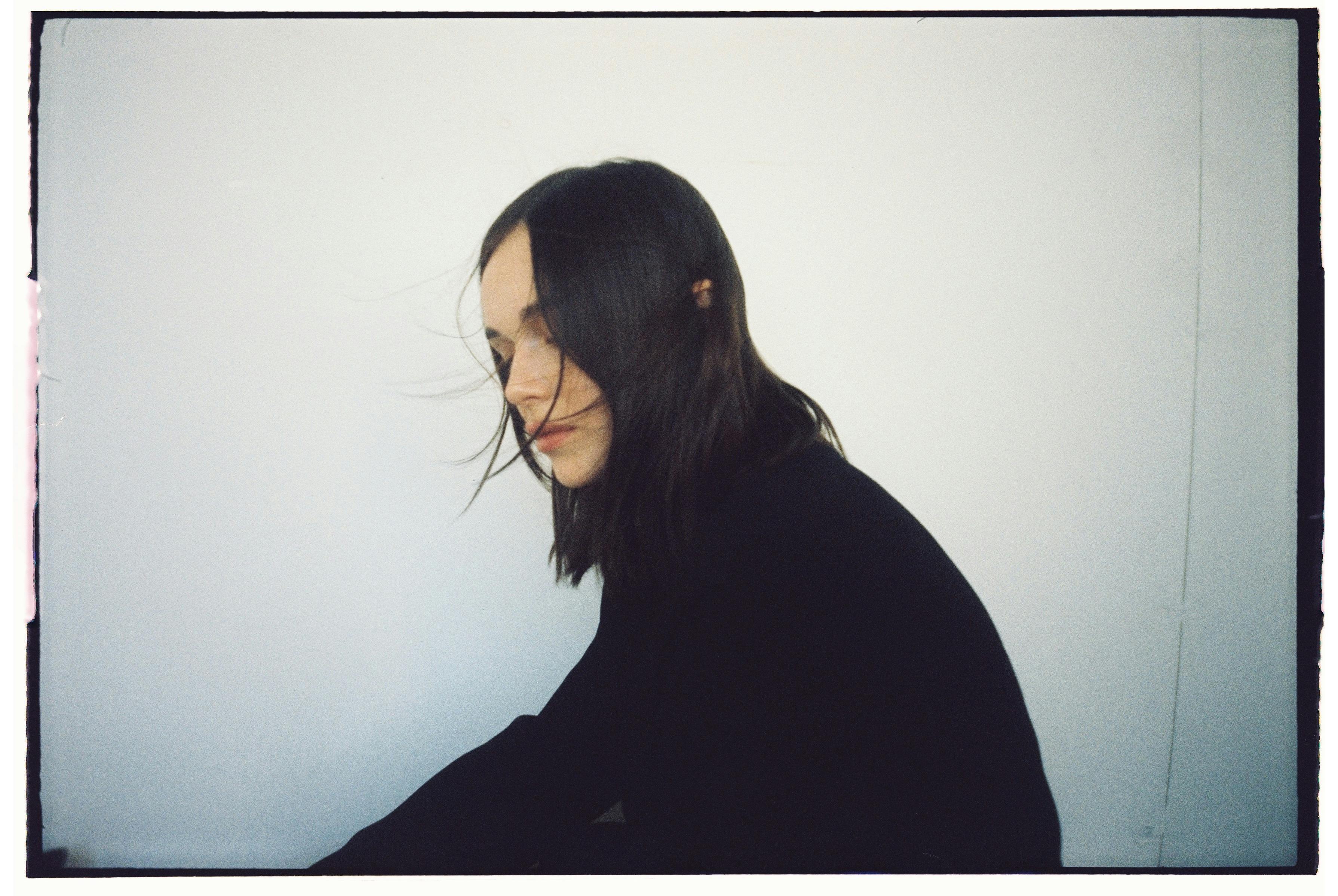 Stylish portrait of a woman in black with hair blowing slightly against a white backdrop.