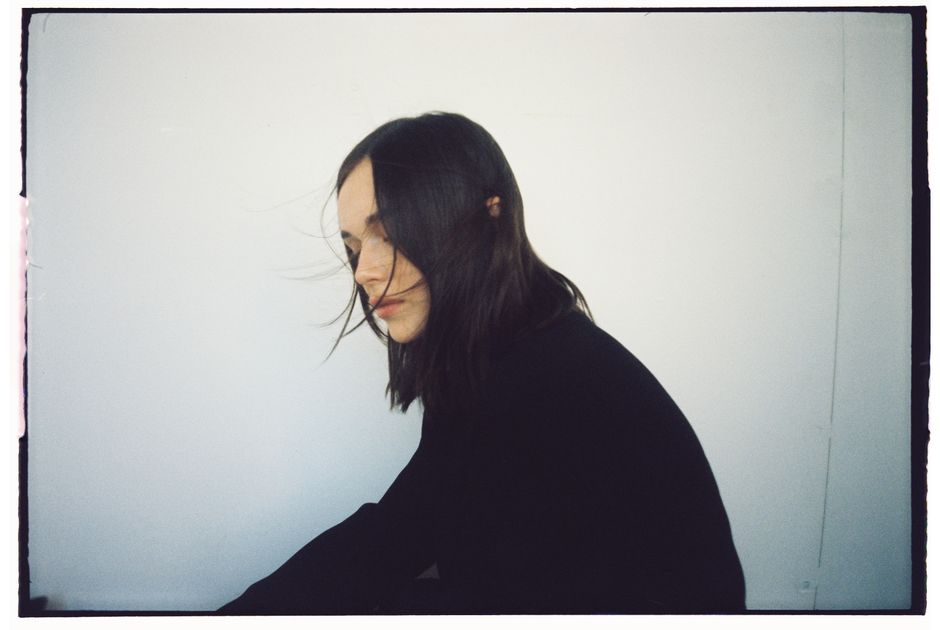 Stylish portrait of a woman in black with hair blowing slightly against a white backdrop.