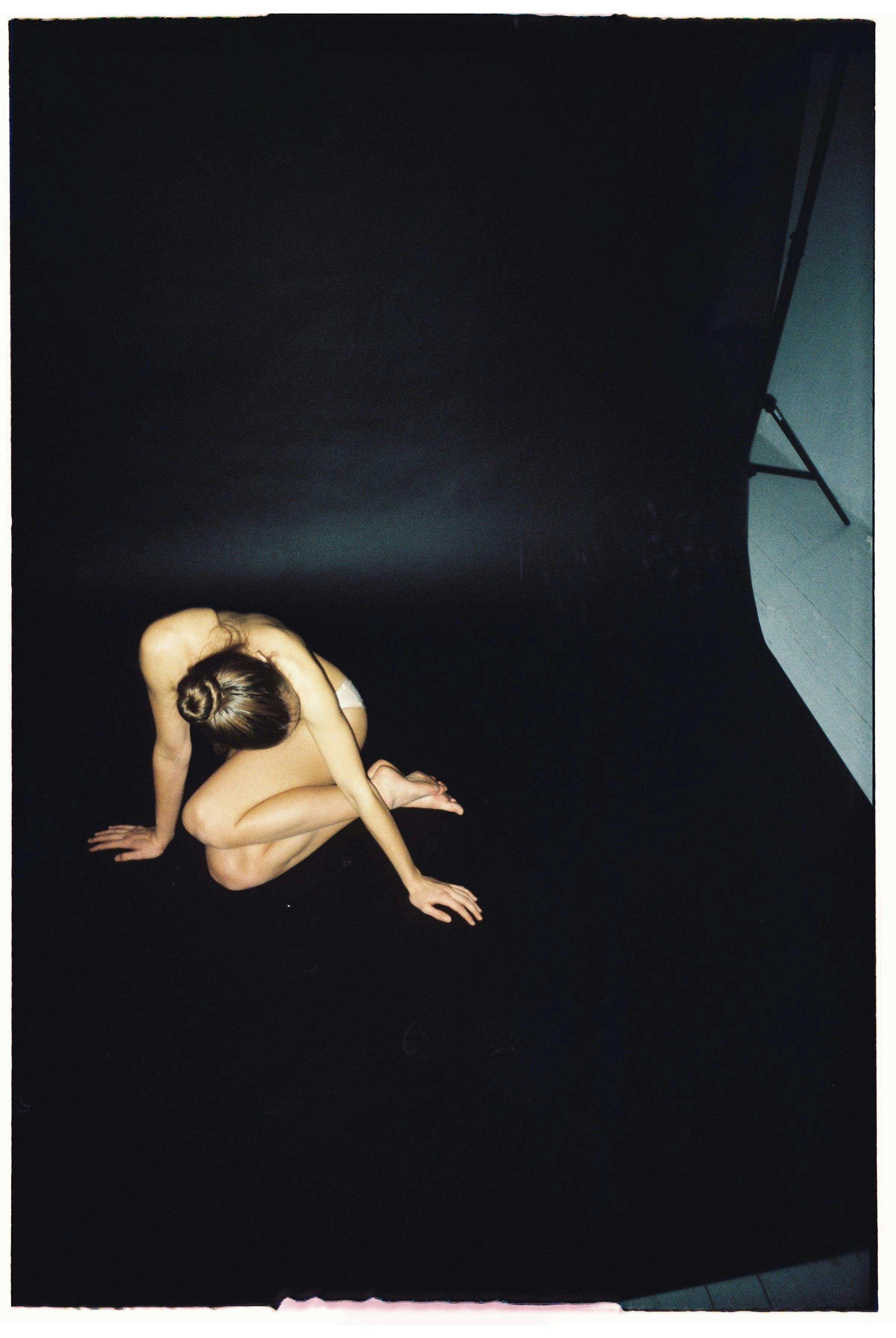 A high-angle artistic studio shot featuring a woman sitting gracefully against a black background.