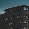 A sleek modern office building with illuminated windows captured at dusk against a moody sky.