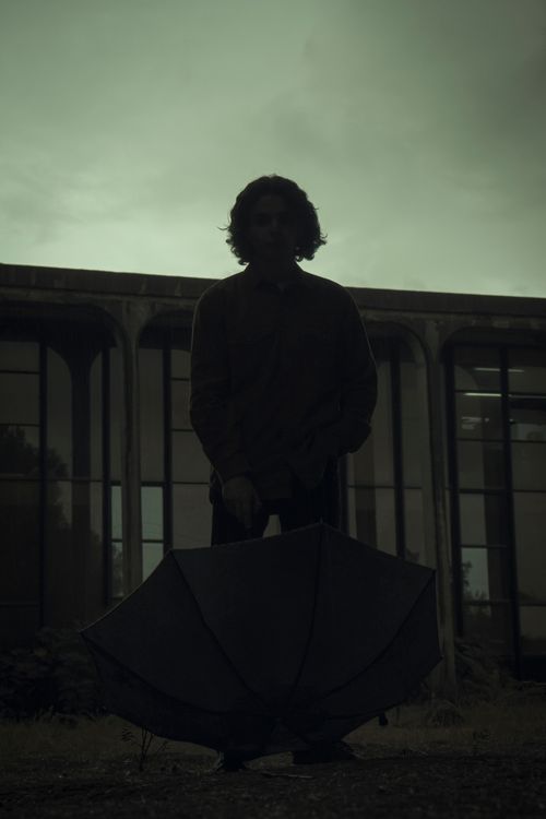 Free A teenager silhouetted against a building, holding an umbrella on a cloudy day. Stock Photo