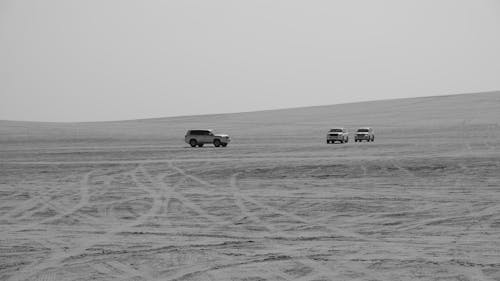 Grayscale Photo of Cars Driving on a Desert